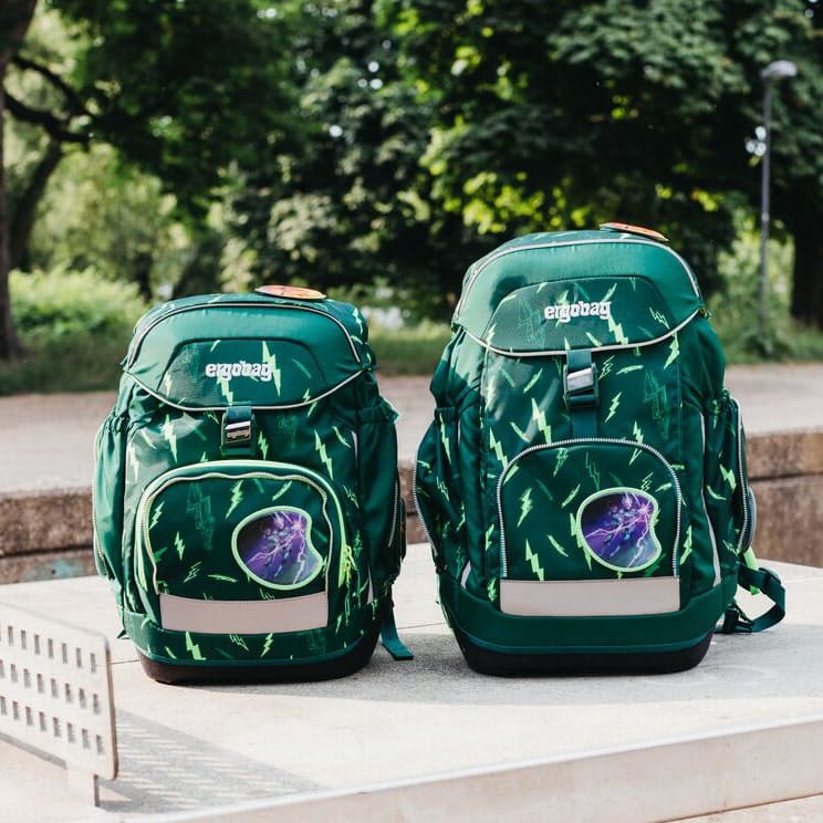 Zwei grüne Ergobag-Schulrucksäcke mit Blitzmuster stehen draußen auf einer Steinoberfläche.